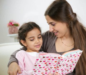 Cute little girl reading book with mother